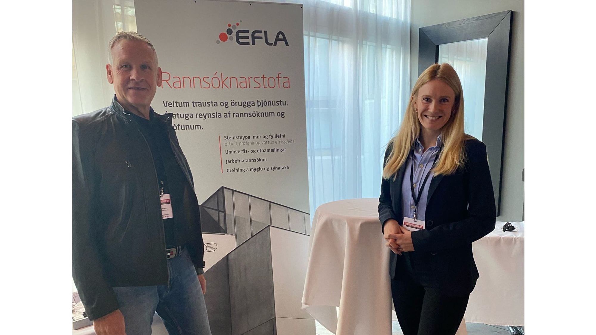 Two individuals standing in a room with a banner of EFLA in the background