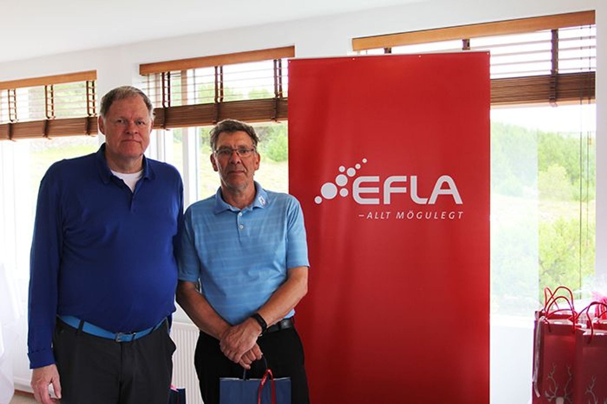 Two men standing in front of a red EFLA promotional banner