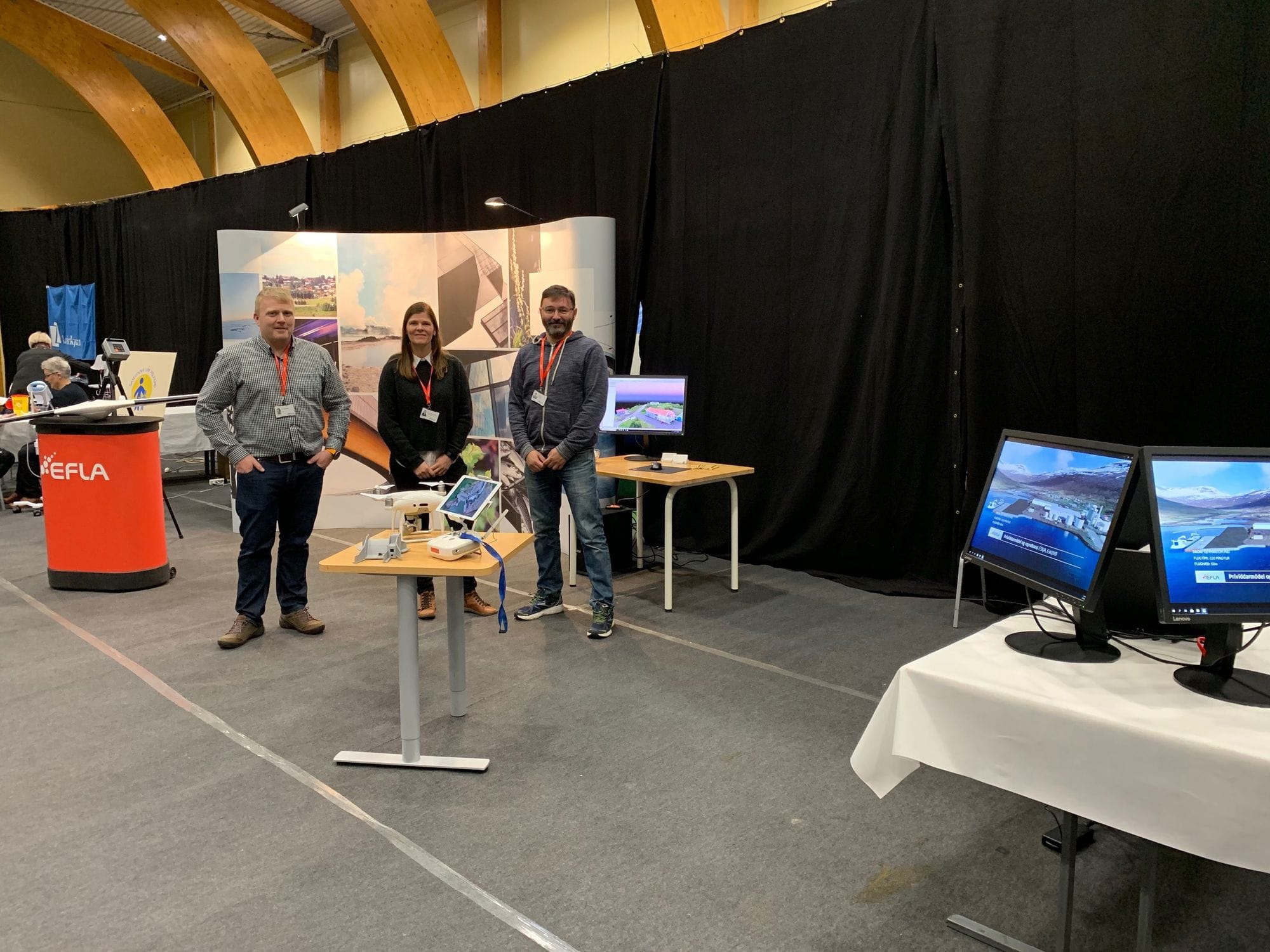 Three individuals standing in a booth at a tech event with many monitors on display