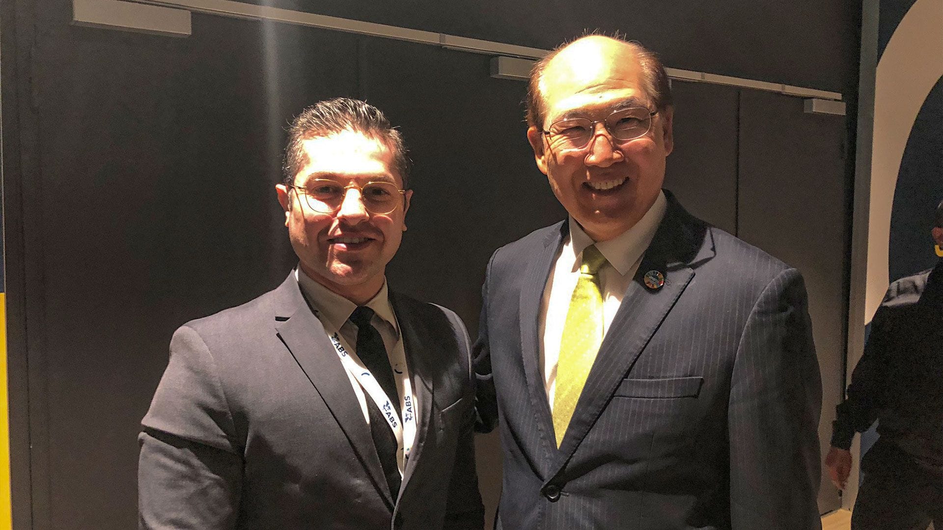 Two men in suit standing close to each other, posing with smile on their faces