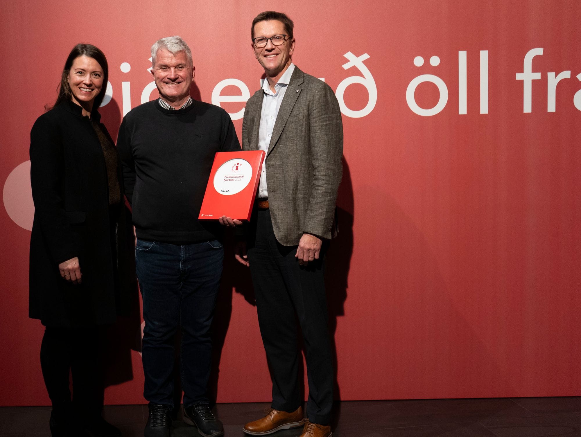 Two men and a women posing with a certificate in front of a red background