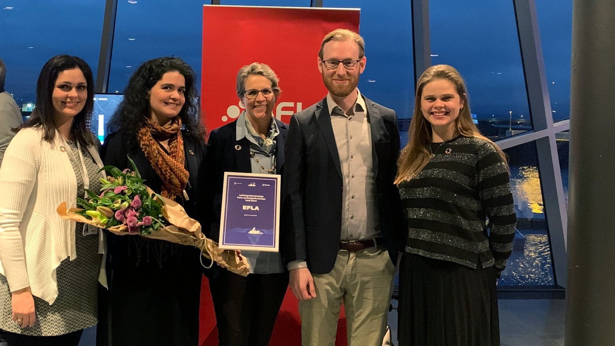 Five individuals standing together, holding certificate and bouquet of flower 