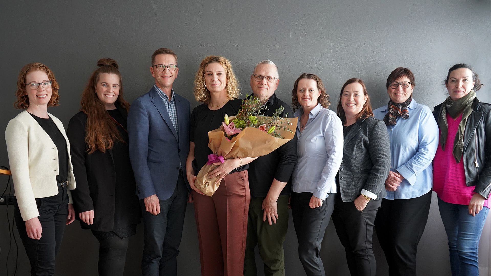 A group of nine people posing for a picture with one person holding a bouquet of flower 