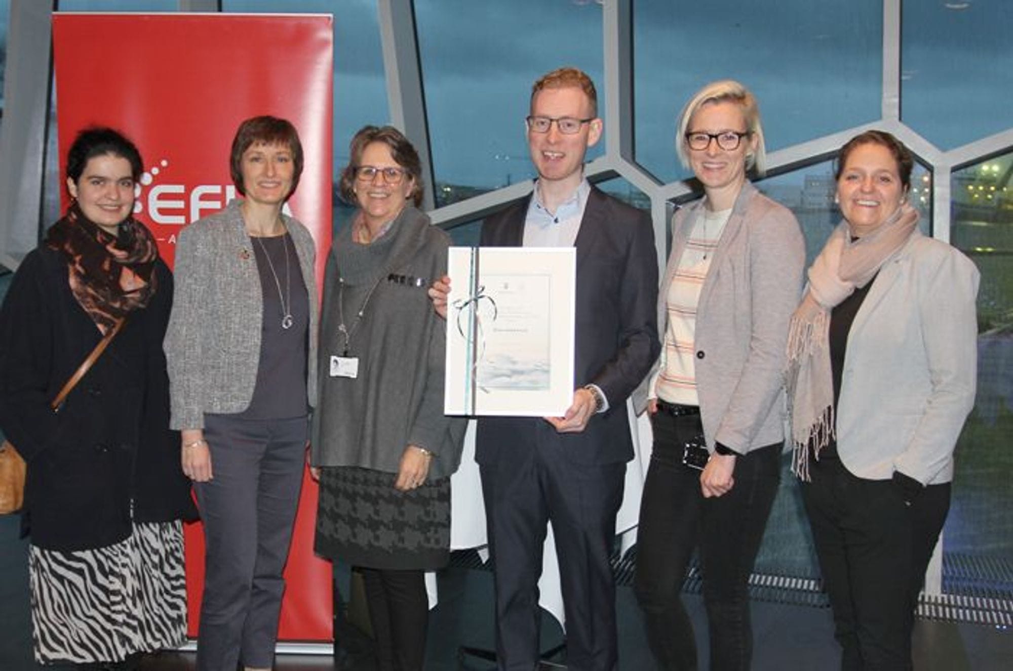 A man is holding a certificate, standing between five women