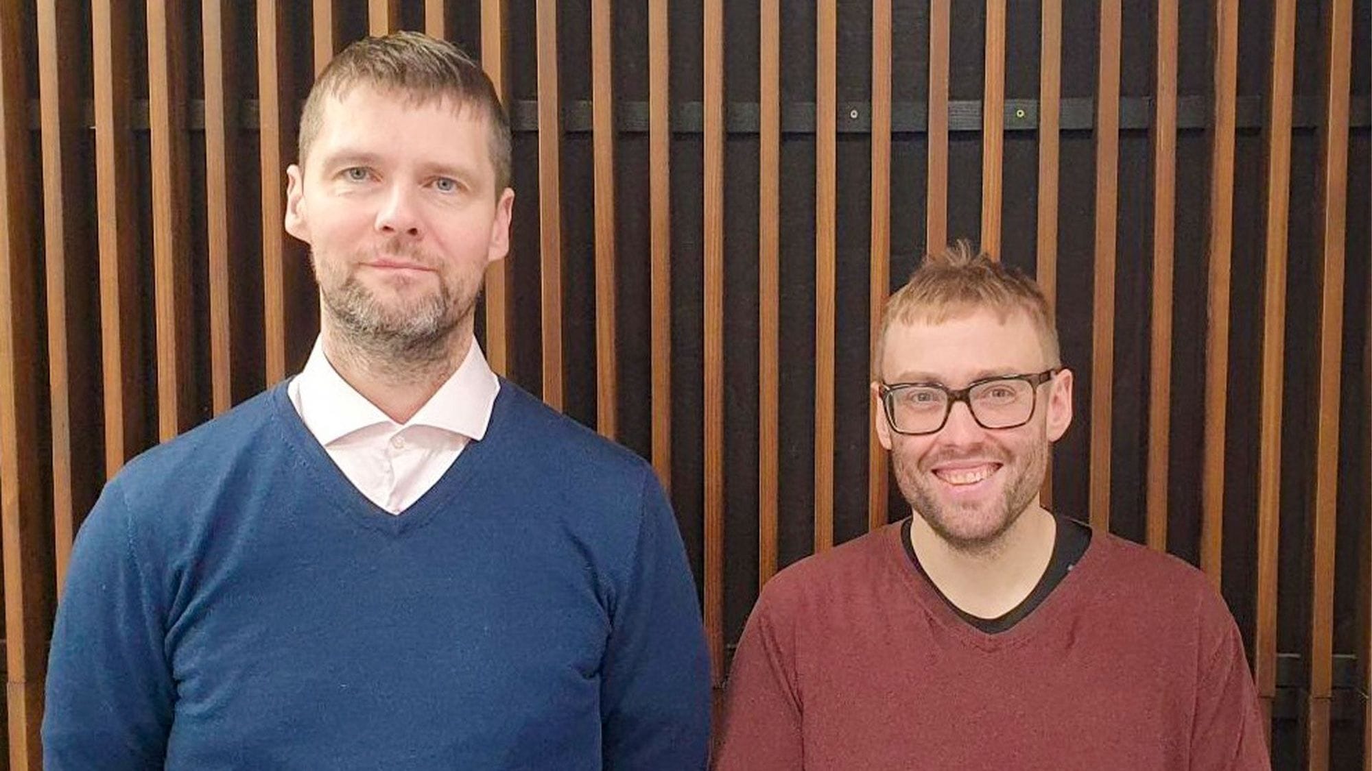 Tveir menn við viðarvegg.