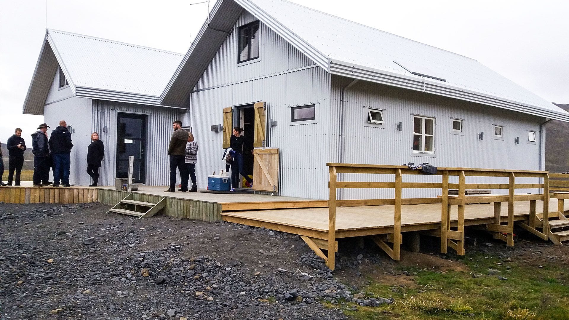 A group of people gathered outside a white building with sloping roof and a wooden deck