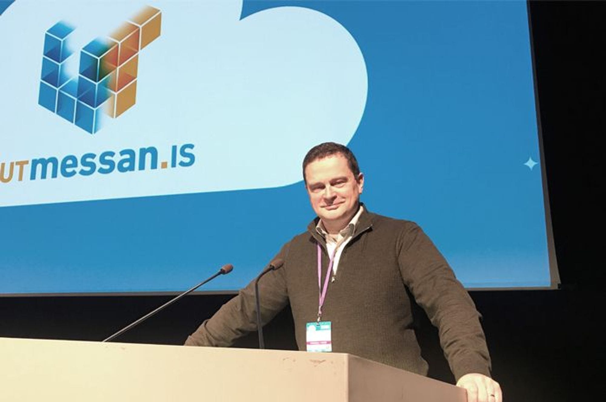 A man smiling at a podium with big screen in the background