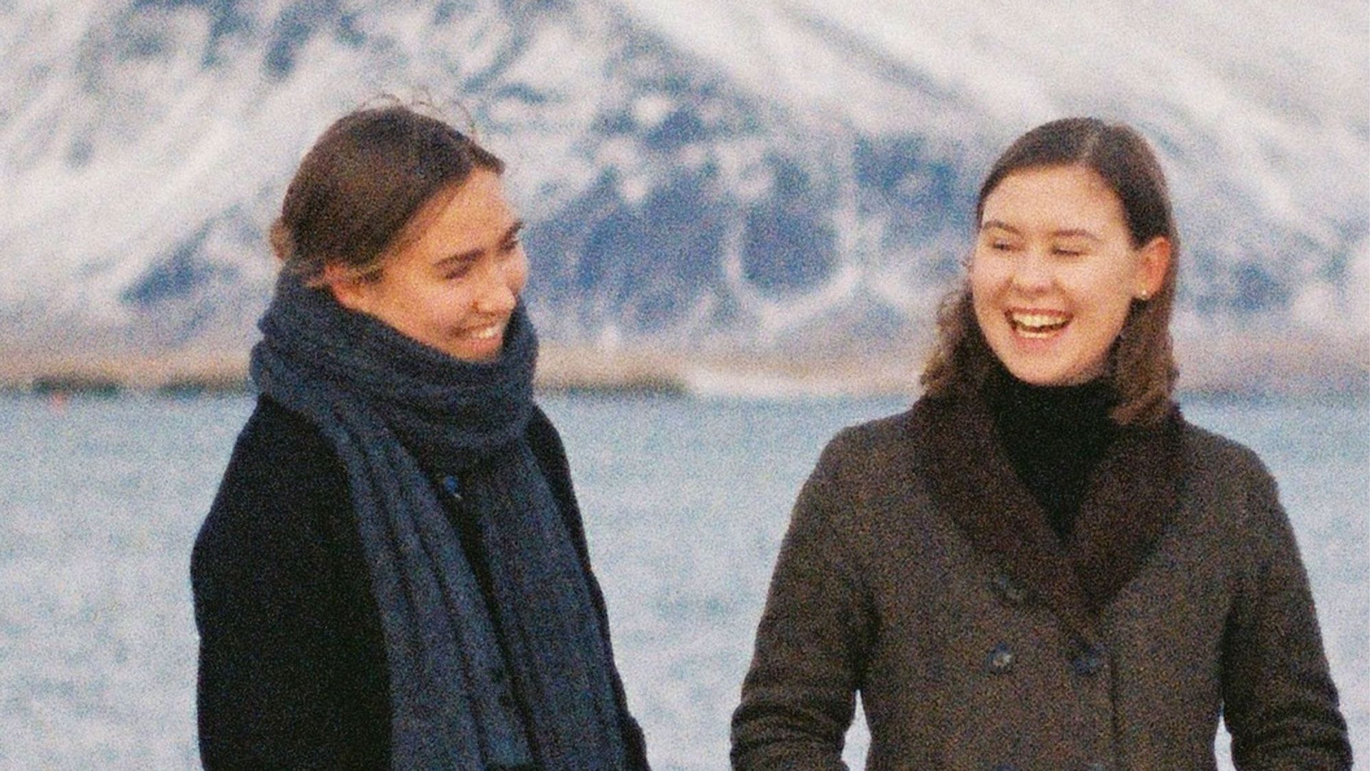 Tvær konur með fjall og haf í baksýn.