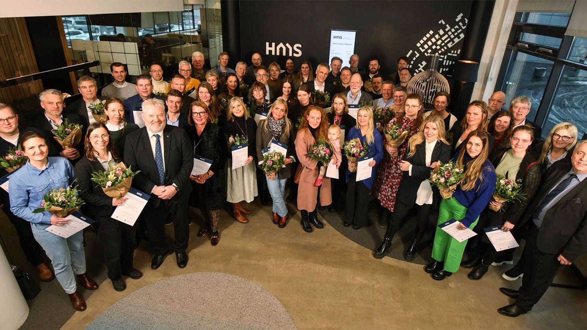 A large group of people holding bouquet of flower and certificates suggesting a celebration