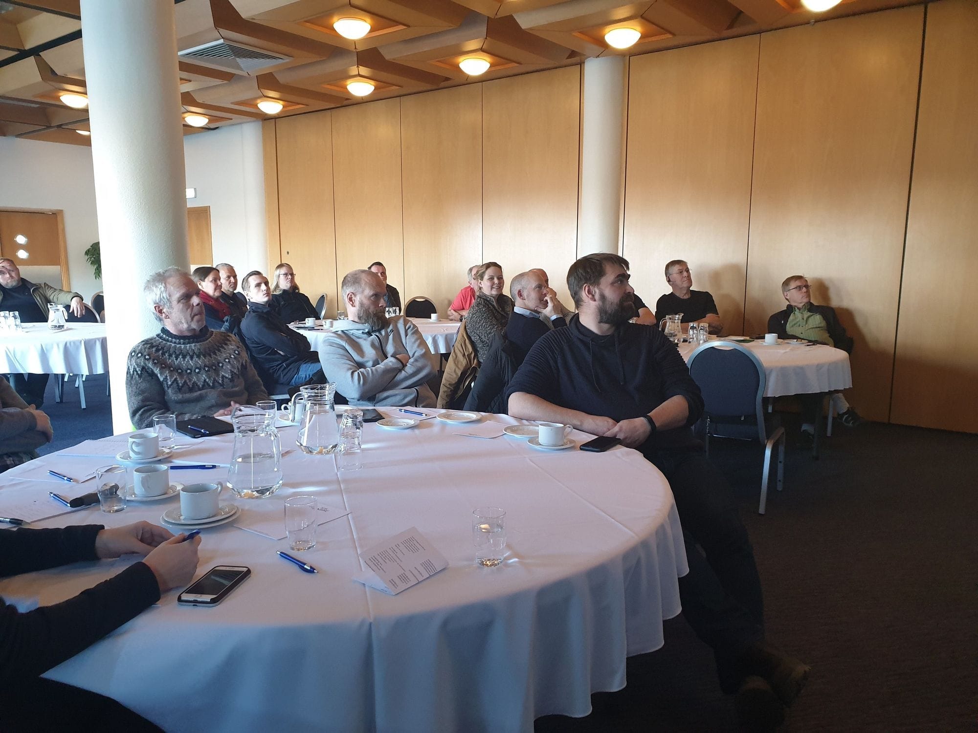 A group of attentive people seated around round tables at a conference 