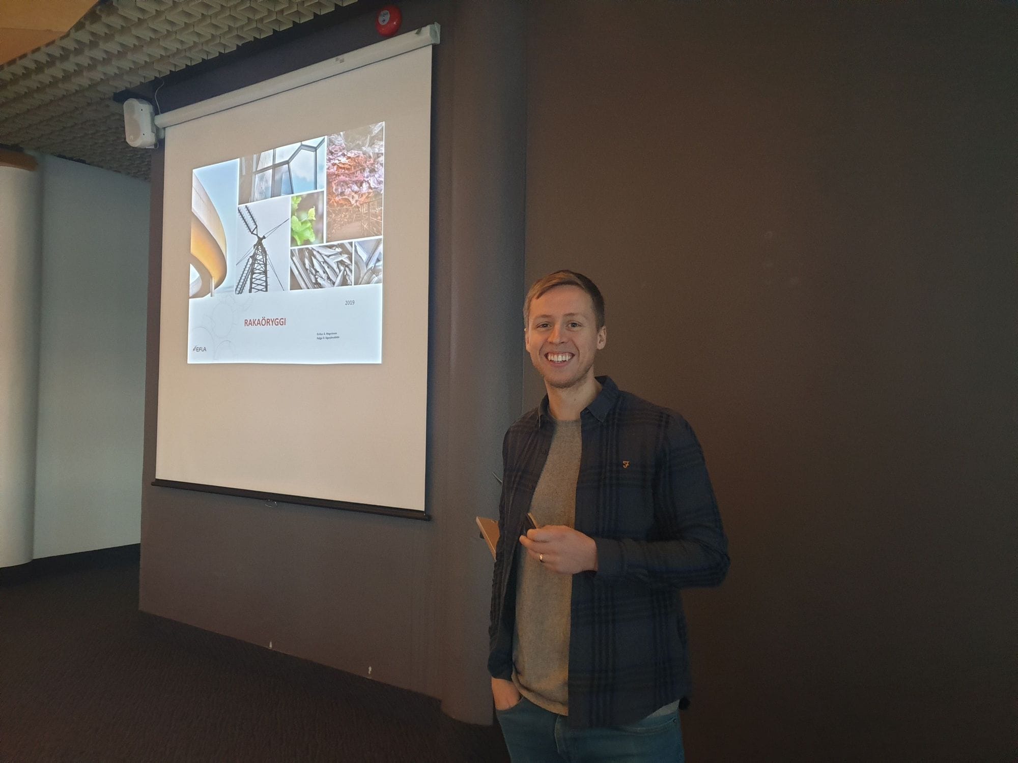 A man standing with a smile next to a big screen with images
