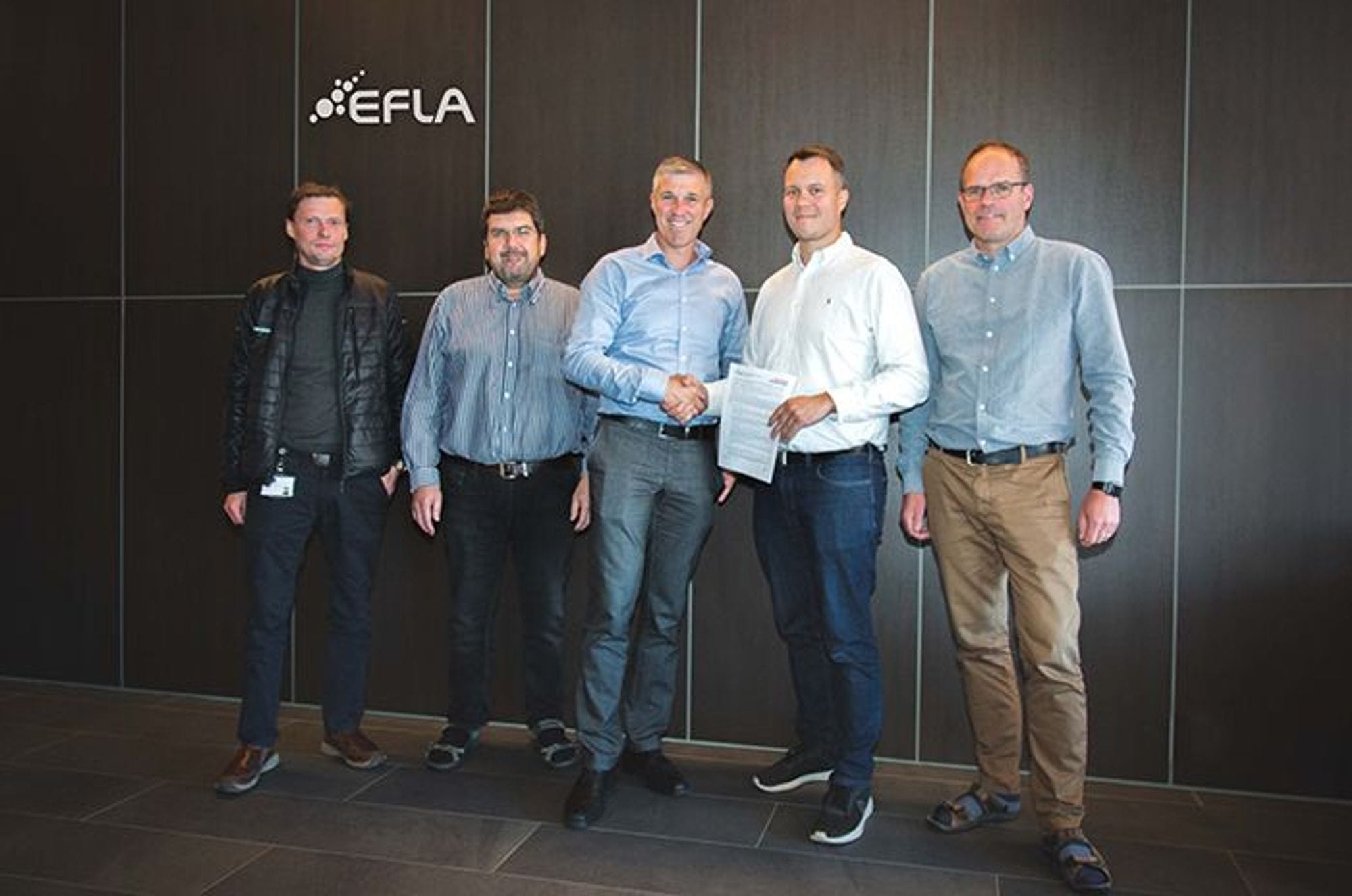 Two men shaking hands and standing between few men, which seems like to seal a deal