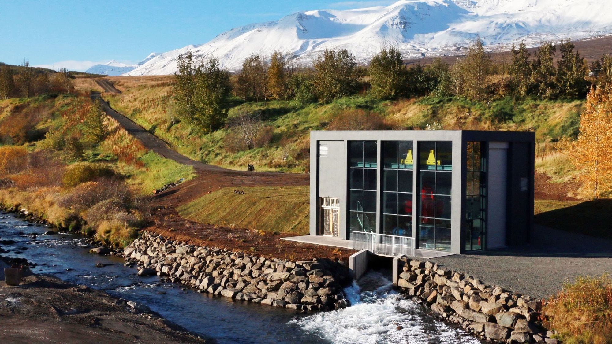 A modern building with large windows next to a river with rocky embankment