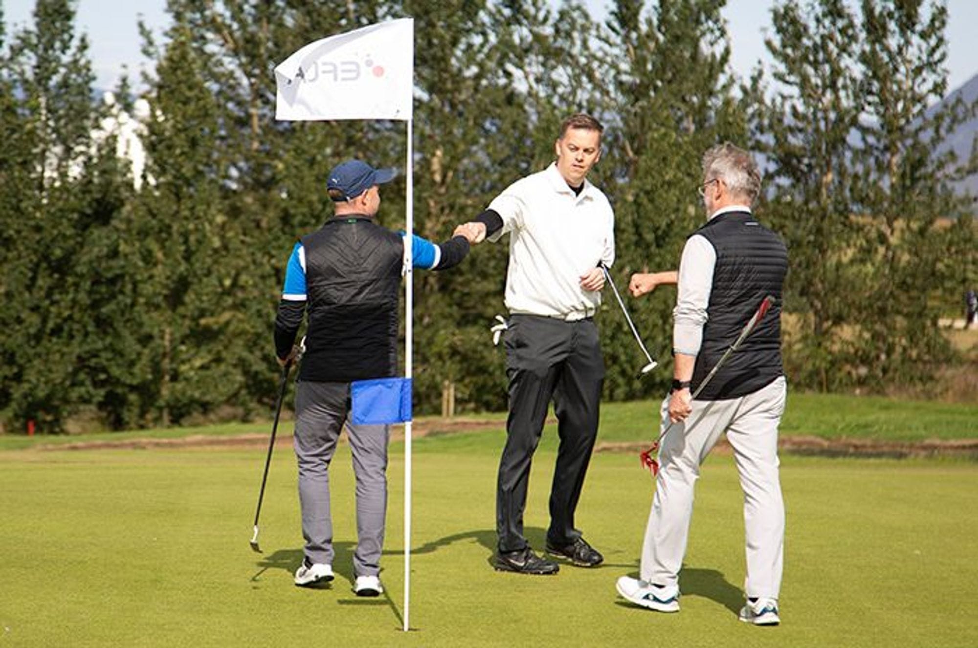 Three men on a golf course holding golf clubs