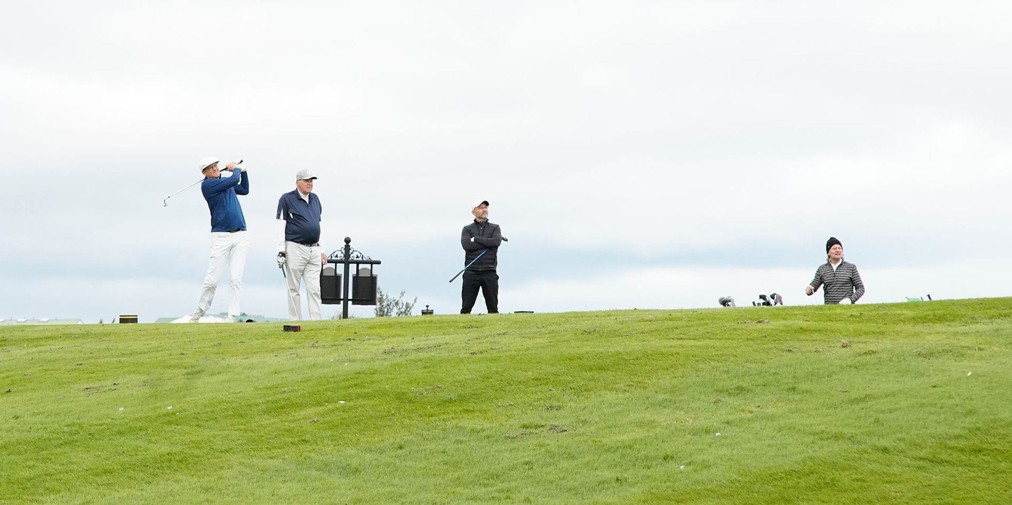 Four golfers on a golf course, one in mid-swing ang the others observing