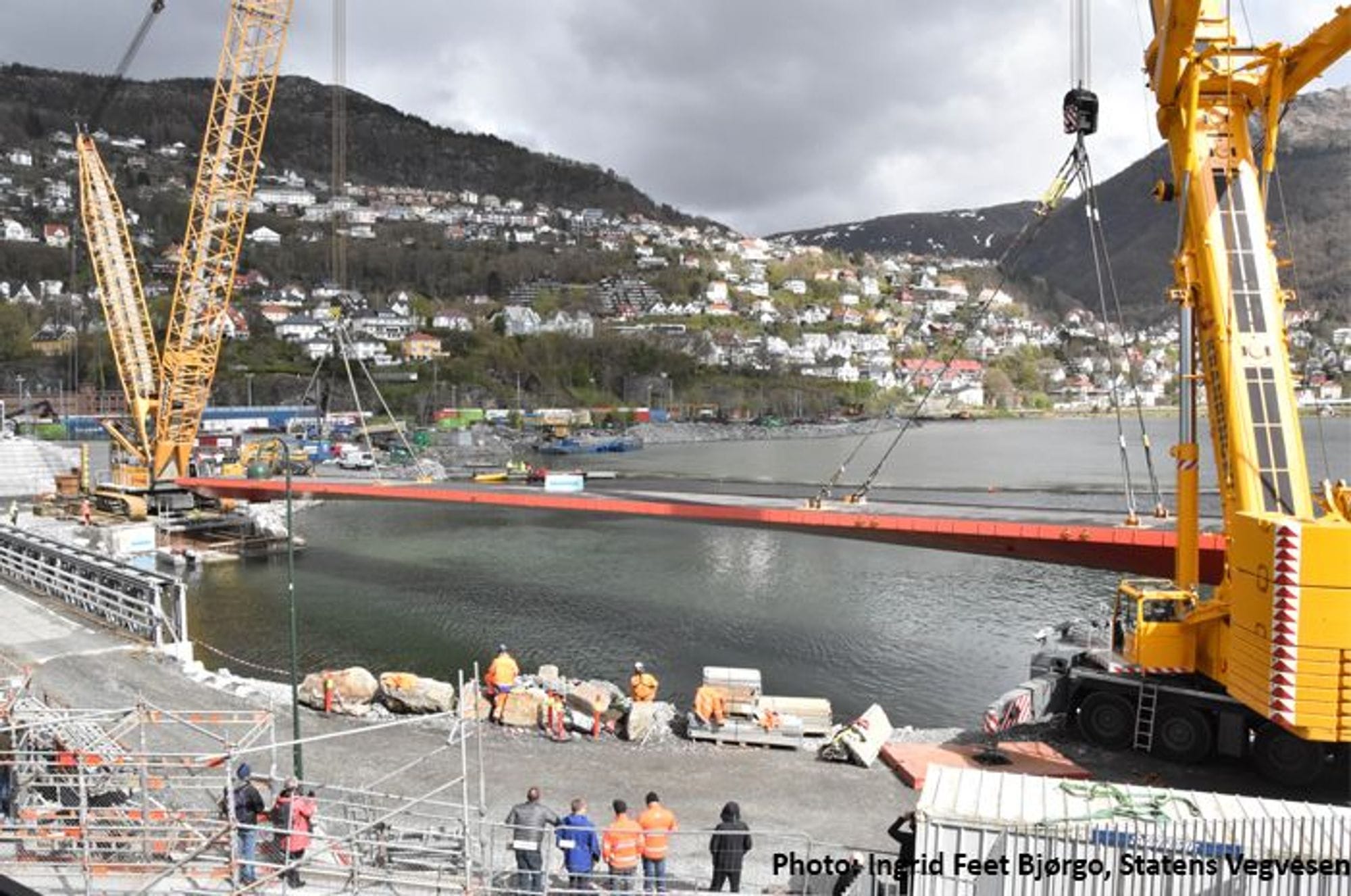 Construction site with a large yellow crane, worker and a part of bridge structure