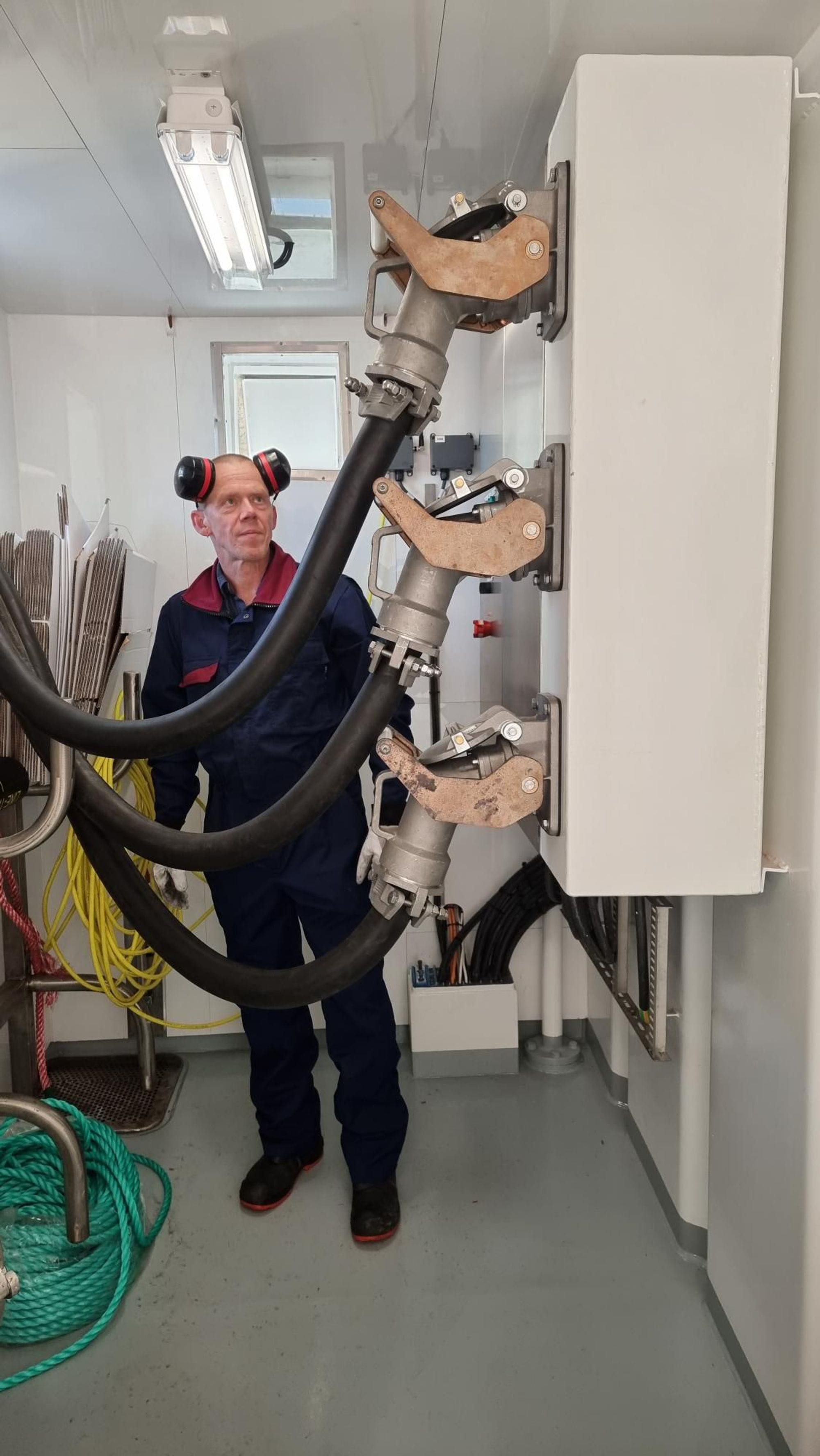 A man in a workshop wearing earmuffs next to thick black industrial cables