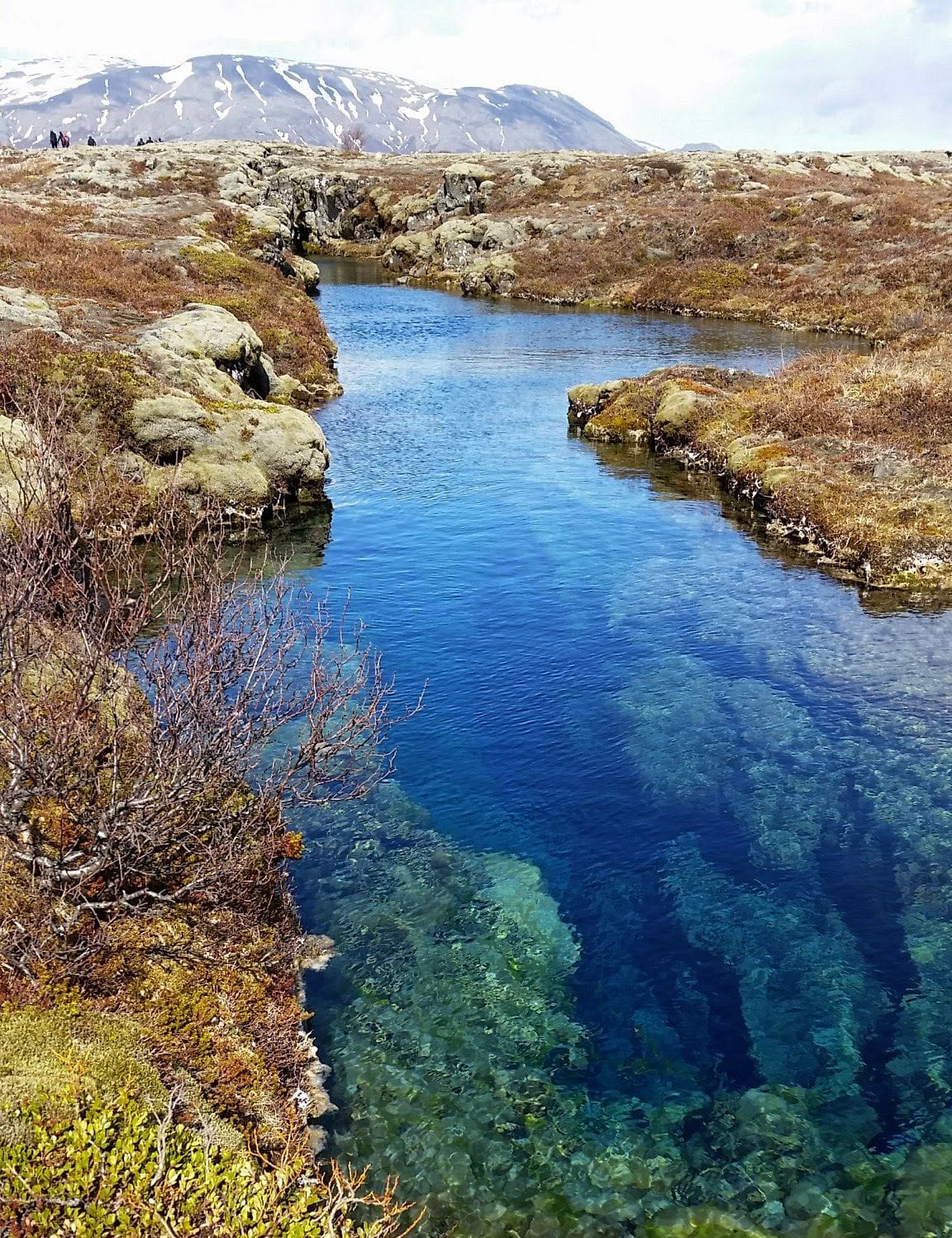 A serene blue water body surrounded by rugged terrain and distant mountains under a hazy sky