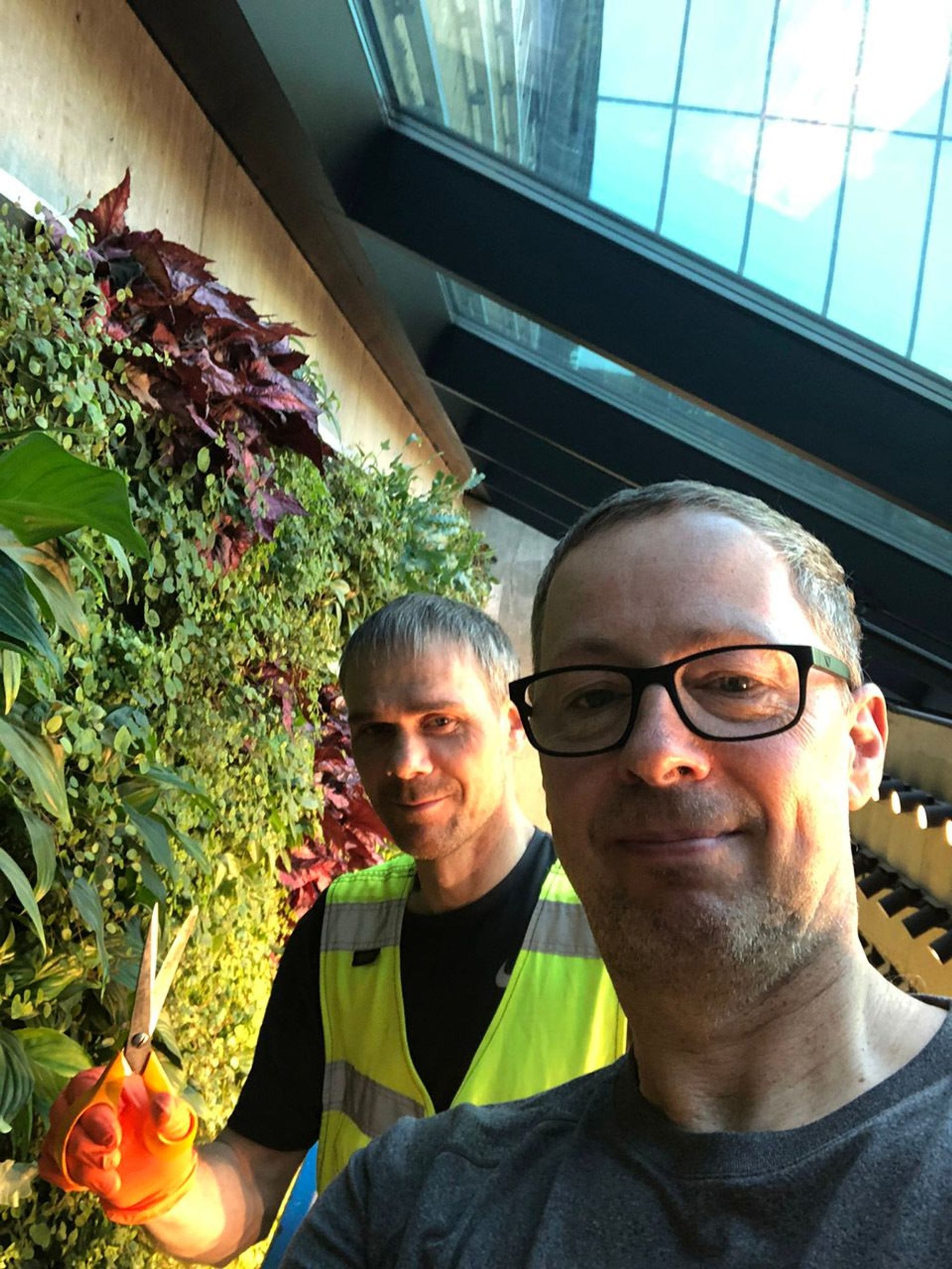 Two men taking a selfie next to a lush vertical garden 