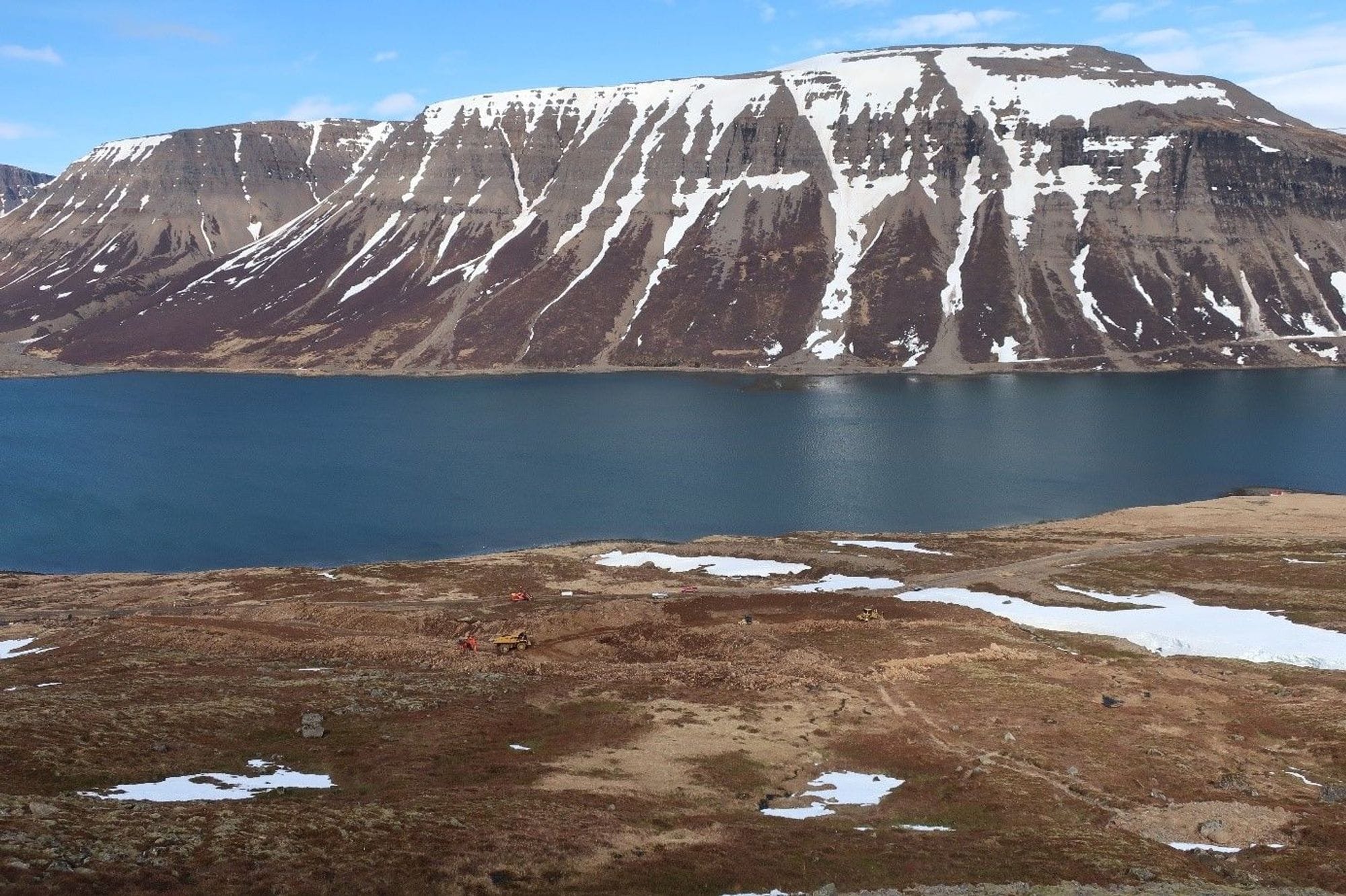 Scenic landscape of a calm blue lake in front of a snow-striped mountain