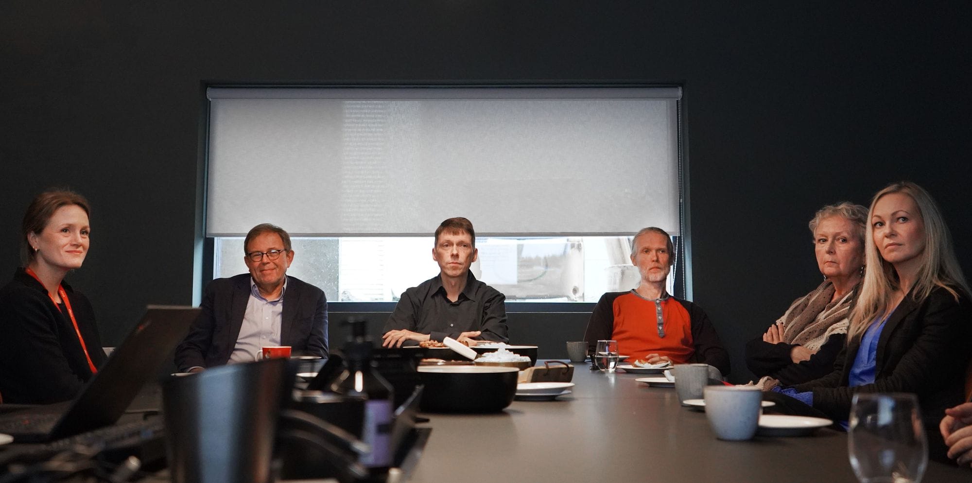 Six individuals seated in a dark room, focused and looking at the same direction
