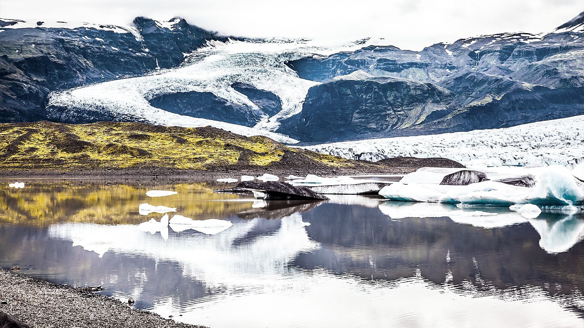 Horft á skriðjökul yfir jökulvatn og mosavaxnar hlíðar við botn jökulsins.