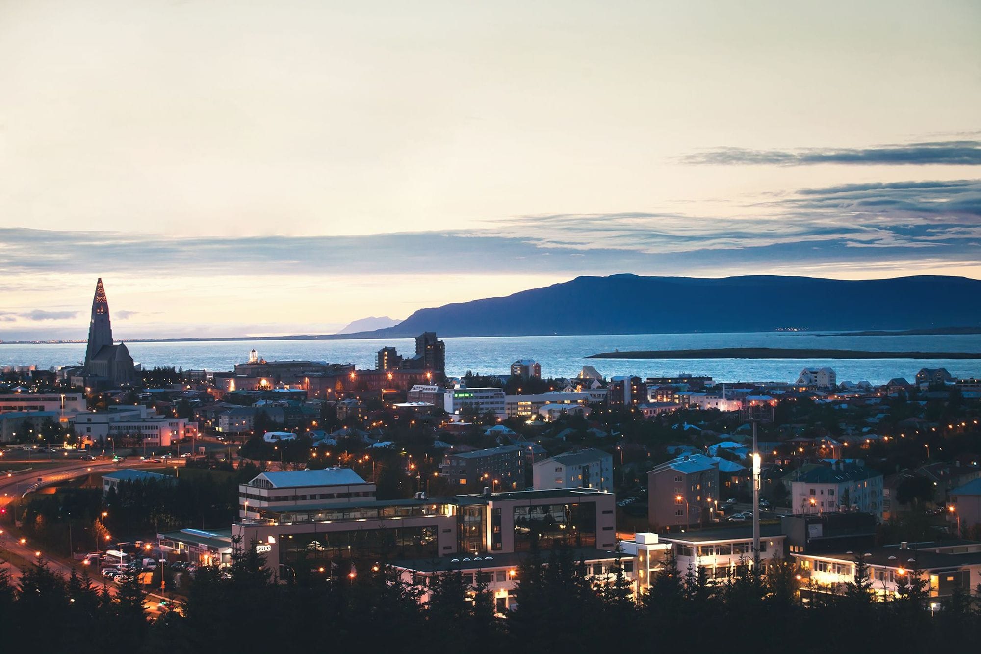 Loftmynd af Reykjavík við sólsetur, sést í Esjuna í bakgrunni