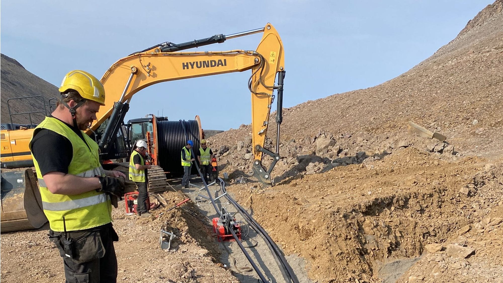 Construction workers in safety gears with an excavator working on pipes