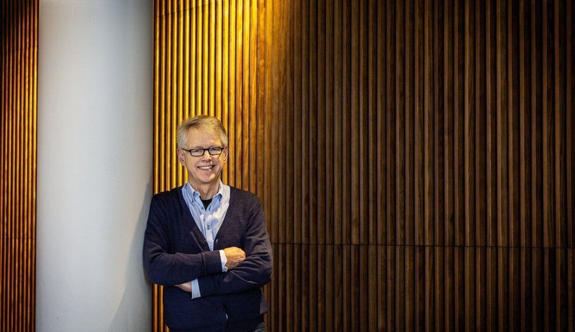 A man standing against a white pillar and vertical wooden salt wall
