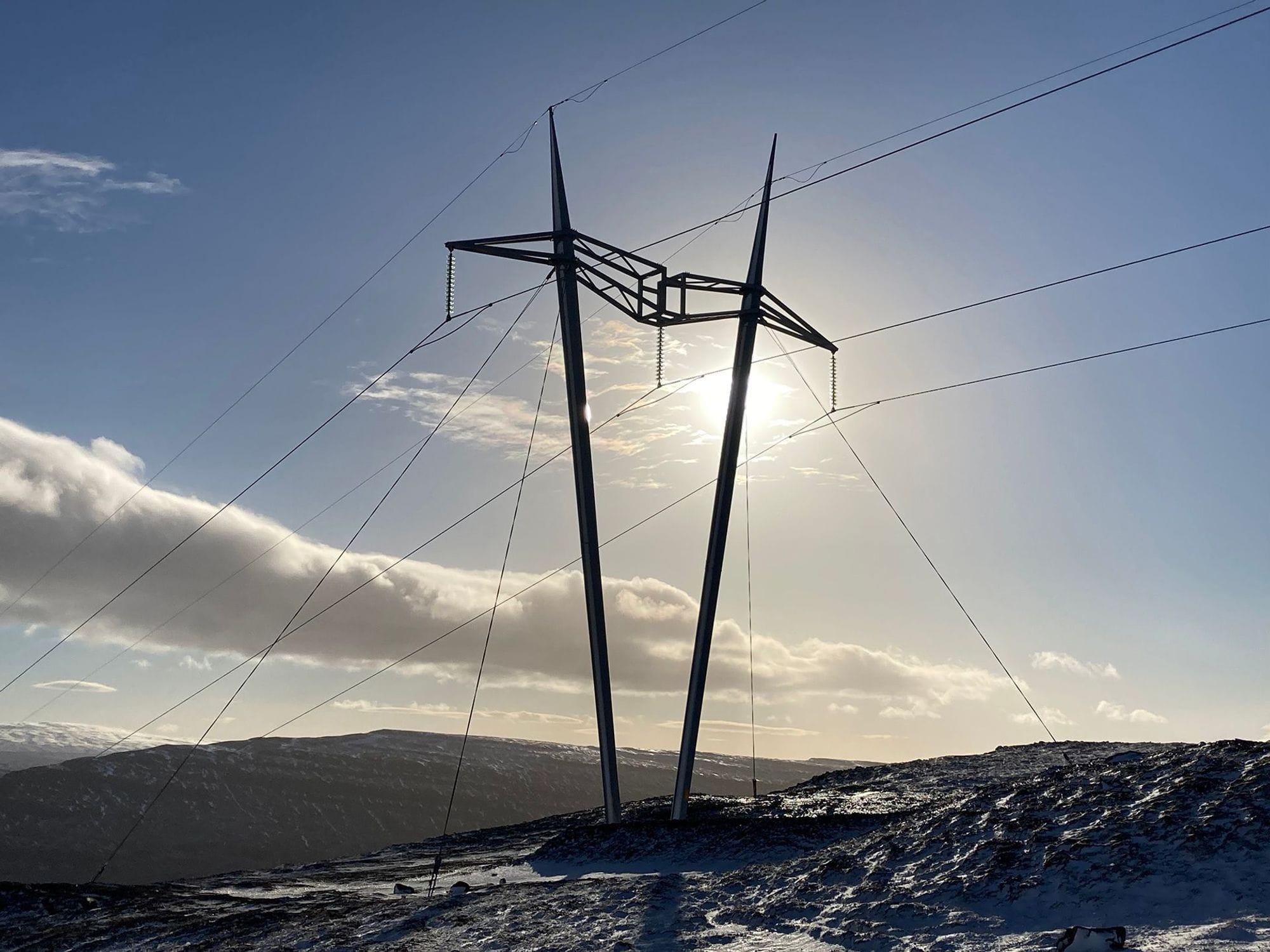 Electricity pylon against bright cloudy sky