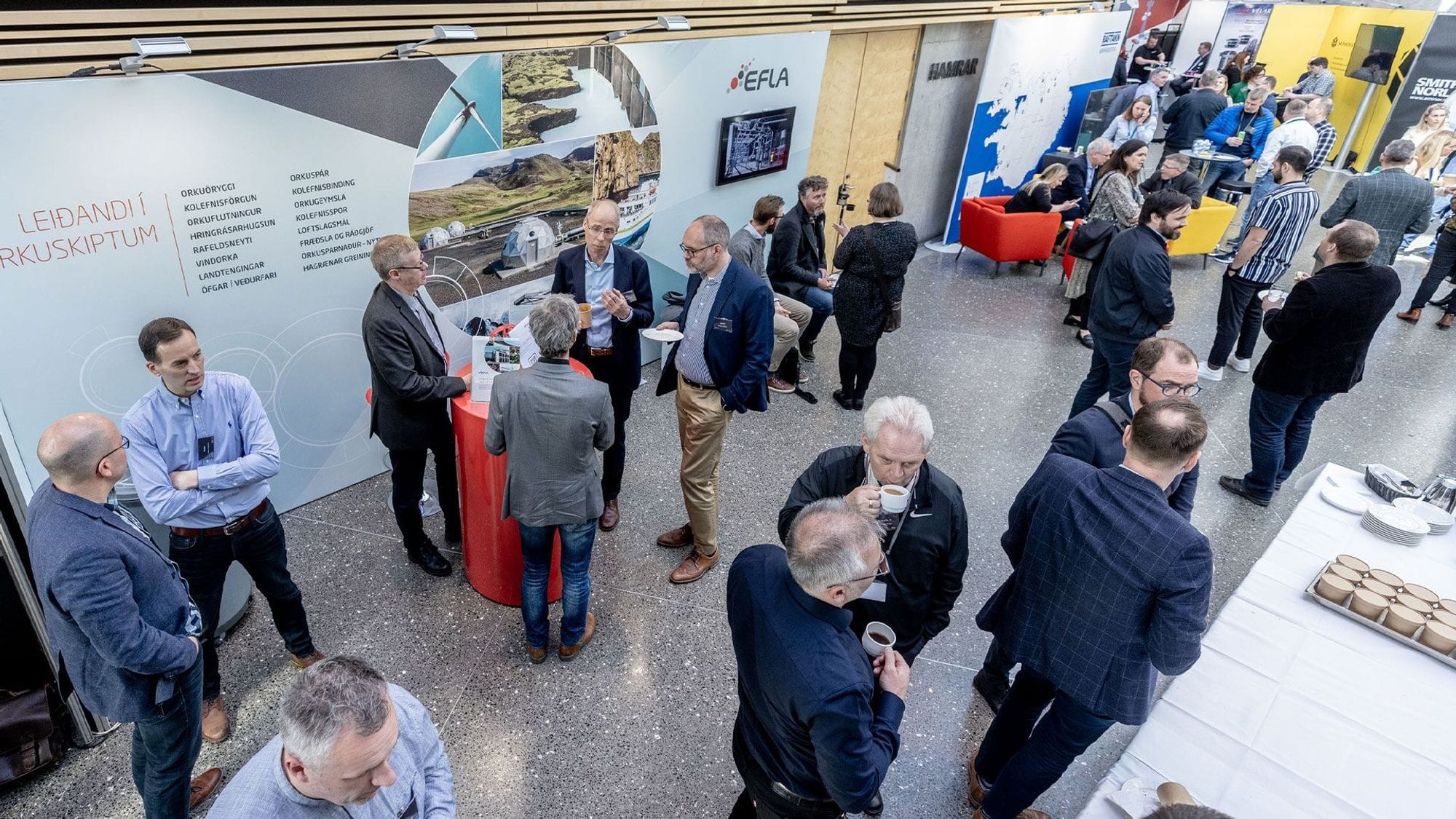 The photo captures a networking event with people conversing and holding drinks with promotional banners