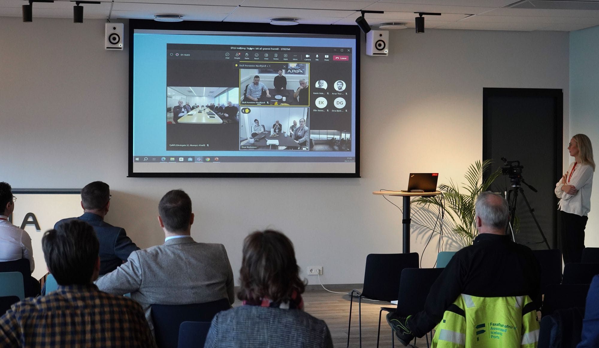 Few individuals watching a big screen which appears to be a video conference call with multiple participant
