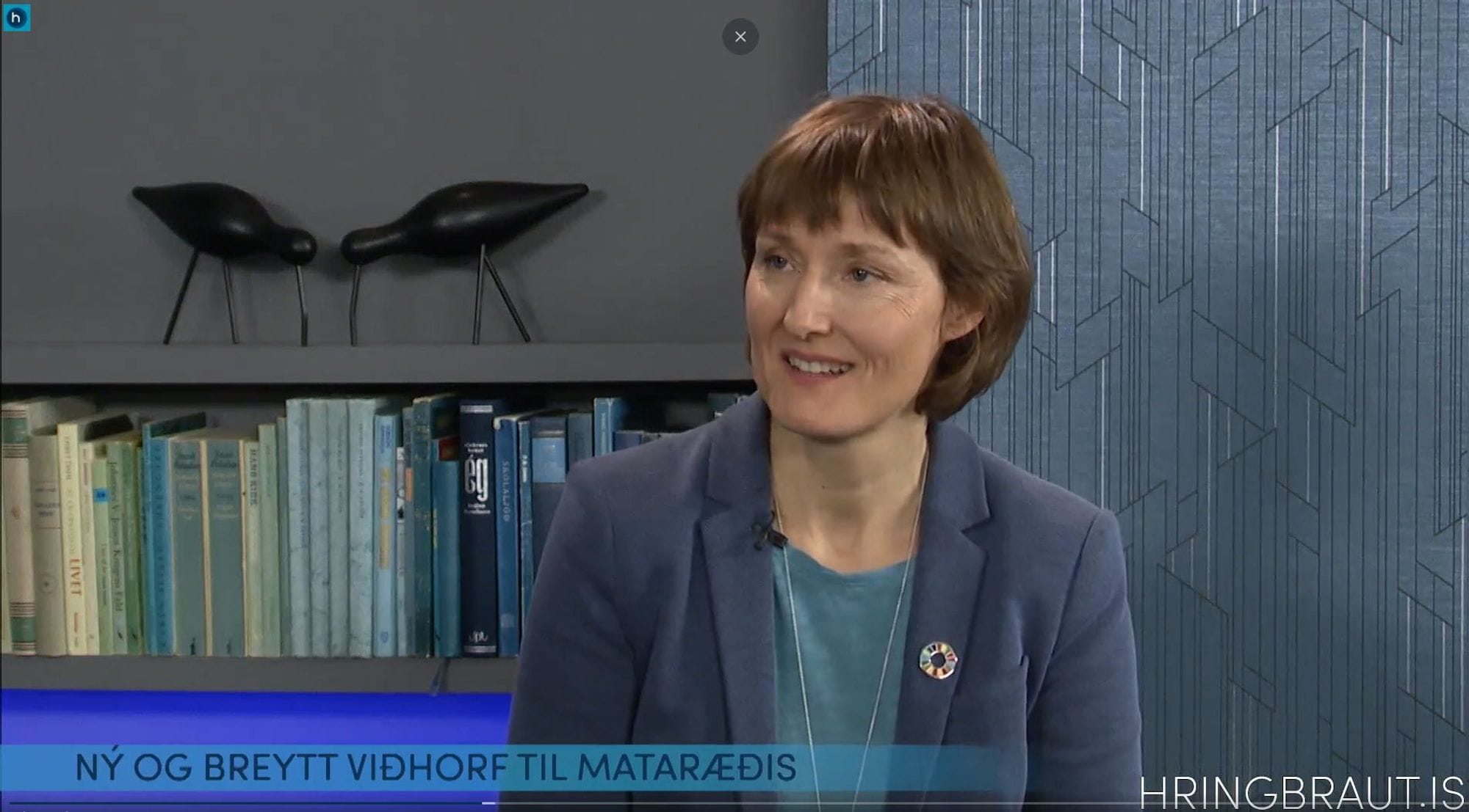 A woman in blue blazer with bookshelf in the background