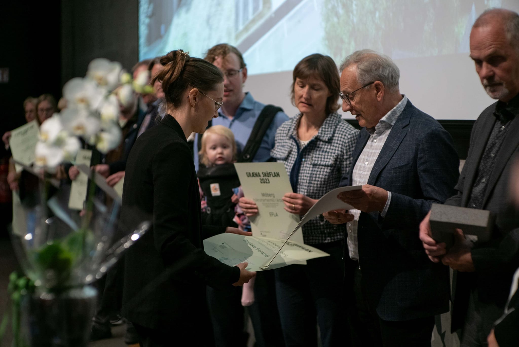 A group of people attentively reading documents or certificate at a ceremony