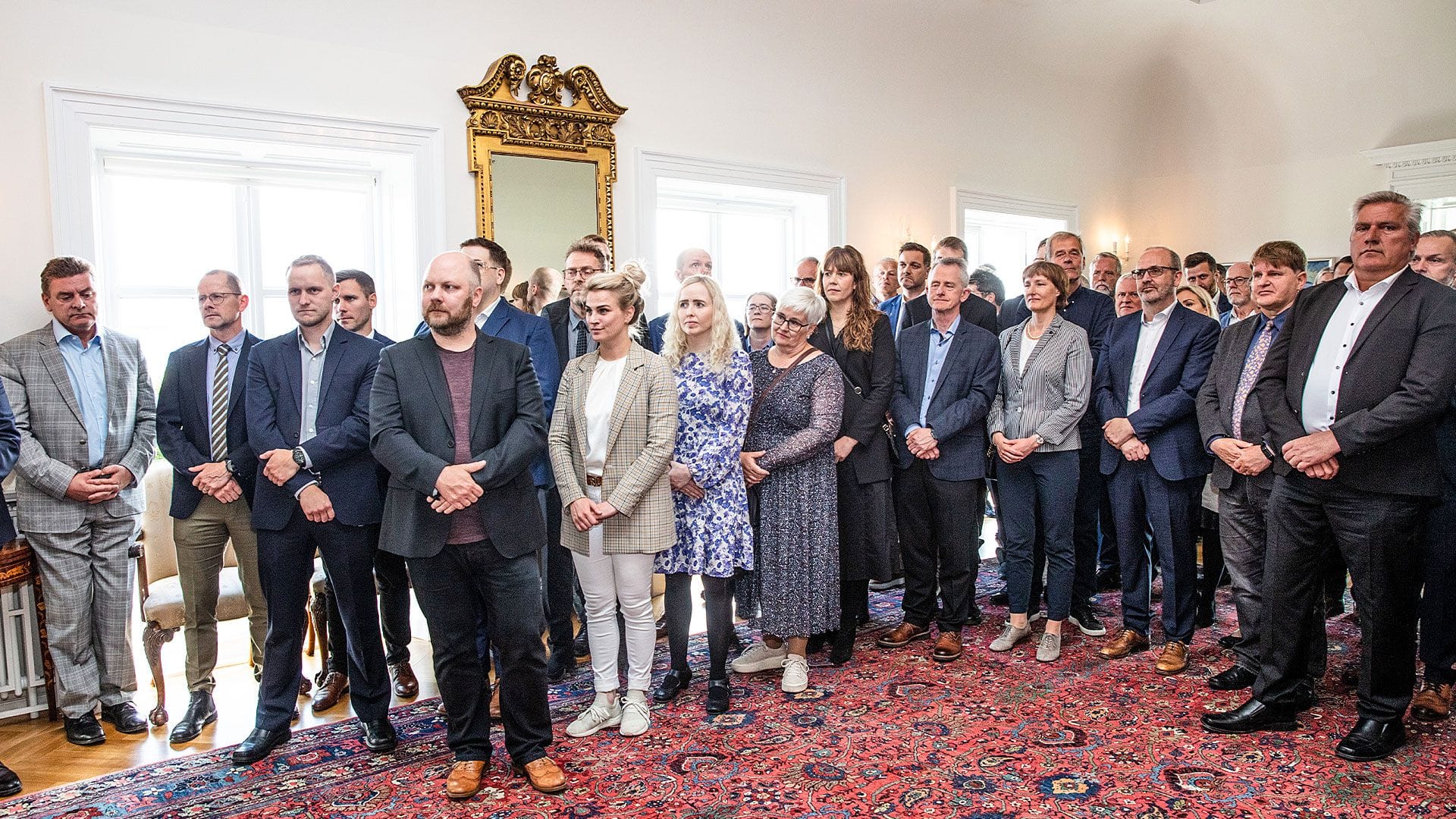 A group of people in a room with ornate decor, all dressed in formal attire 