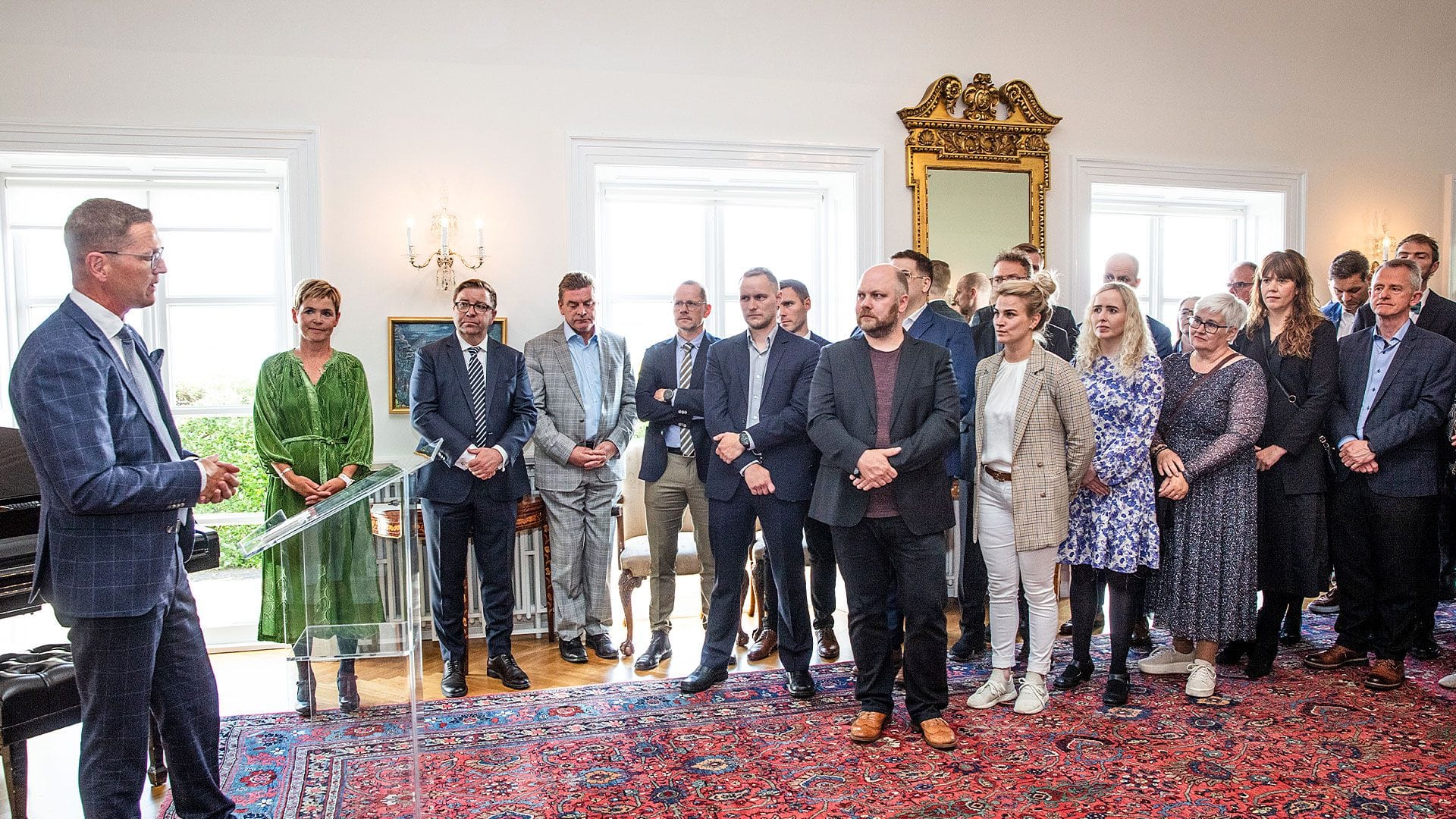 A group of people listening to a speaker in a room with classic decor 