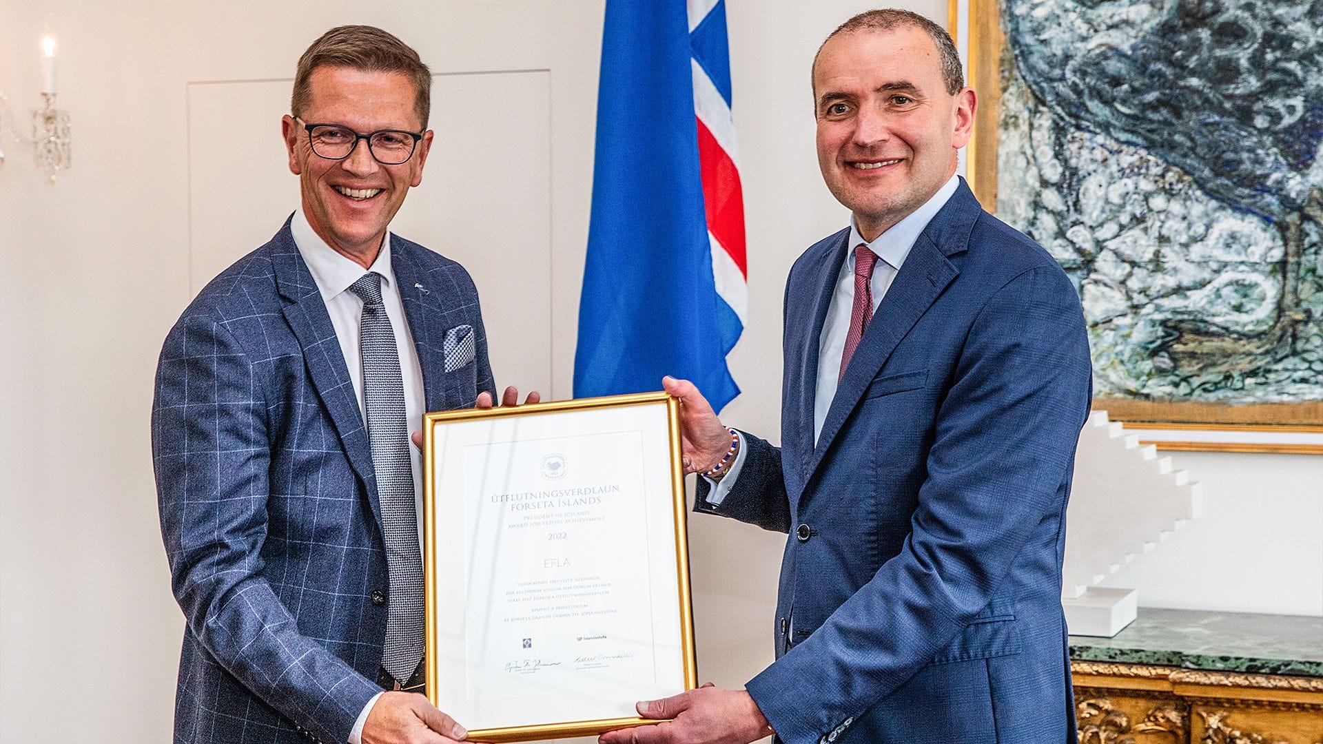 Two men in blue suits holding framed certificate with big smiling faces