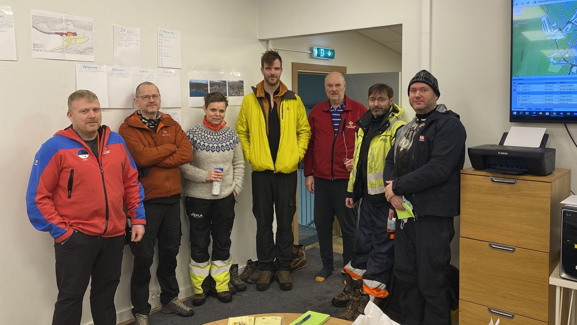 A group of people standing in a room, wearing warm clothing and reflective jackets
