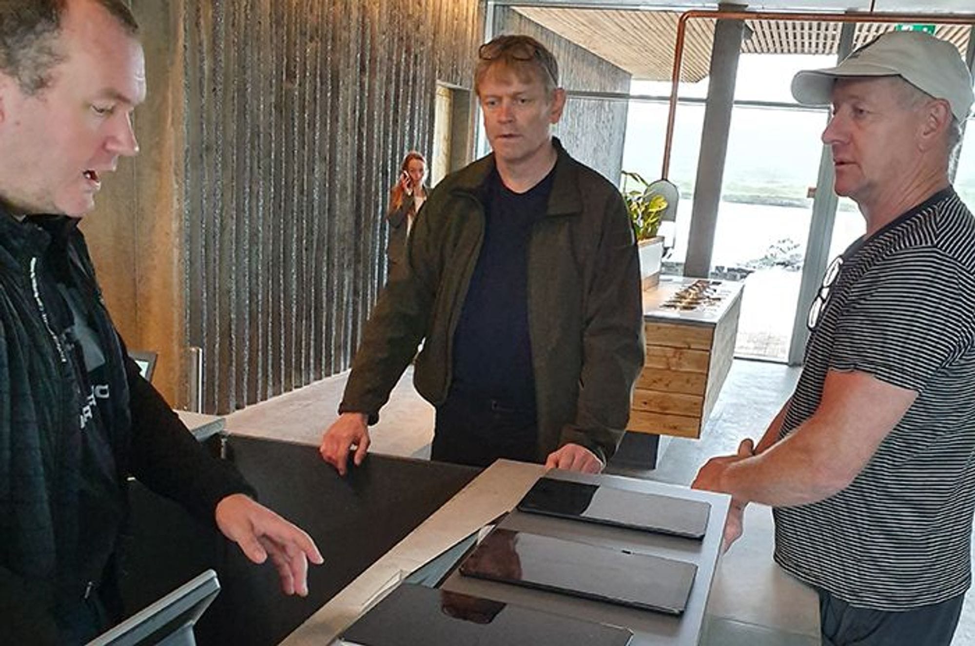 three men engaged in discussion, standing around a table