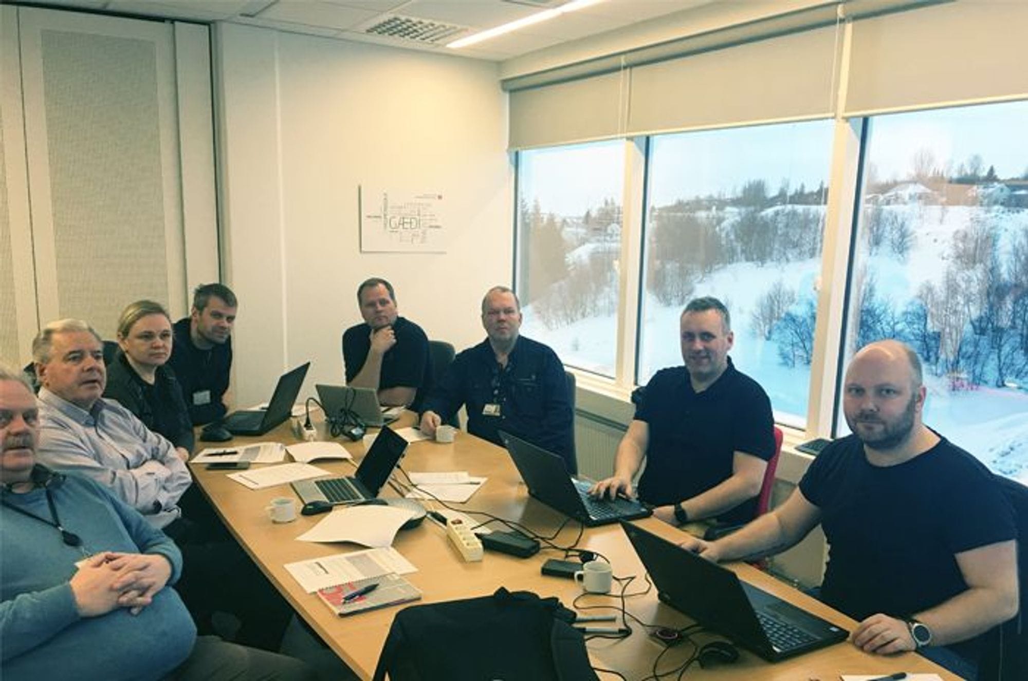  A group of eight people sitting around wooden desk with their laptops open 