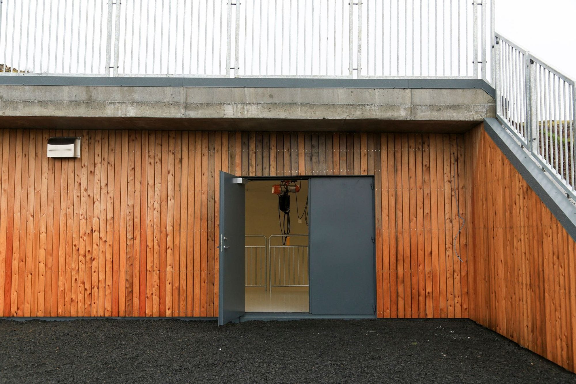 A modern building facade with a wooden exterior, metal door and a staircase leading to an upper level on the right side