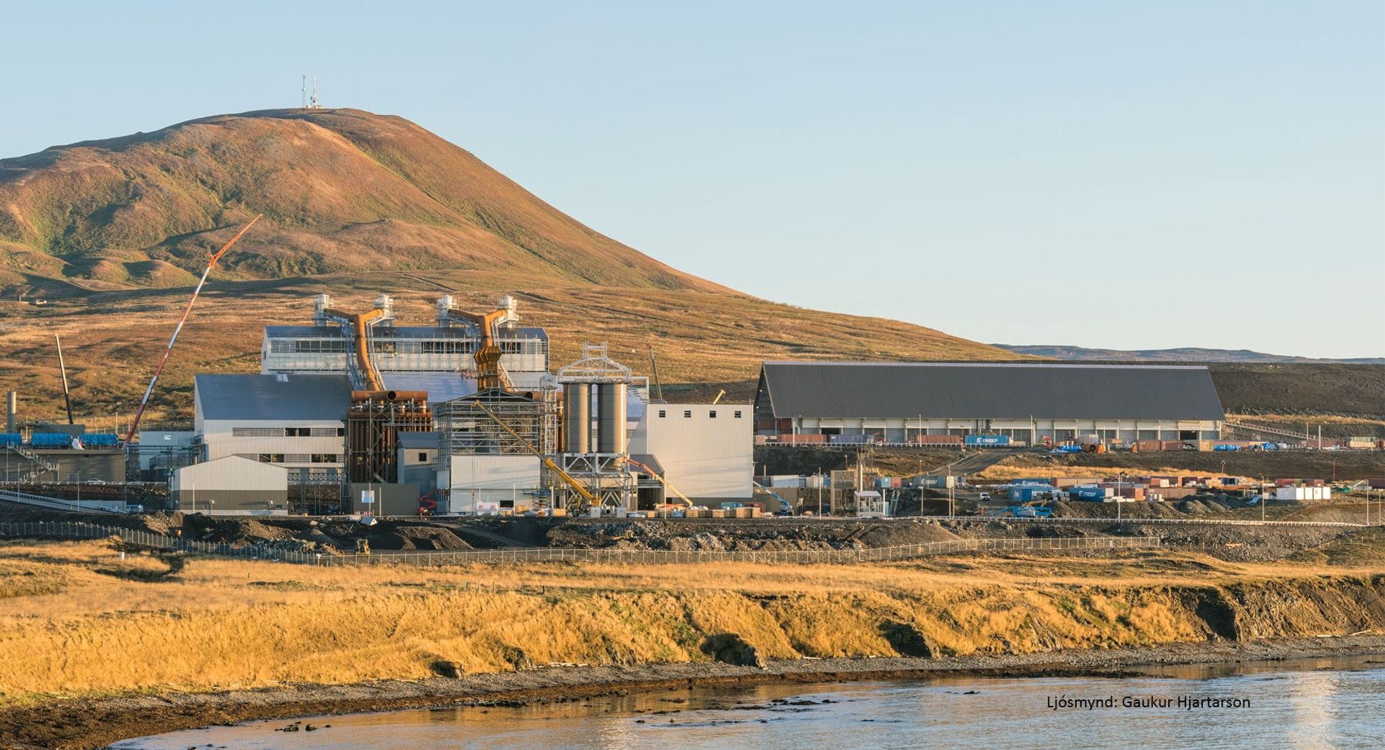 Verksmiðja við ströndina með fjall í baksýn.