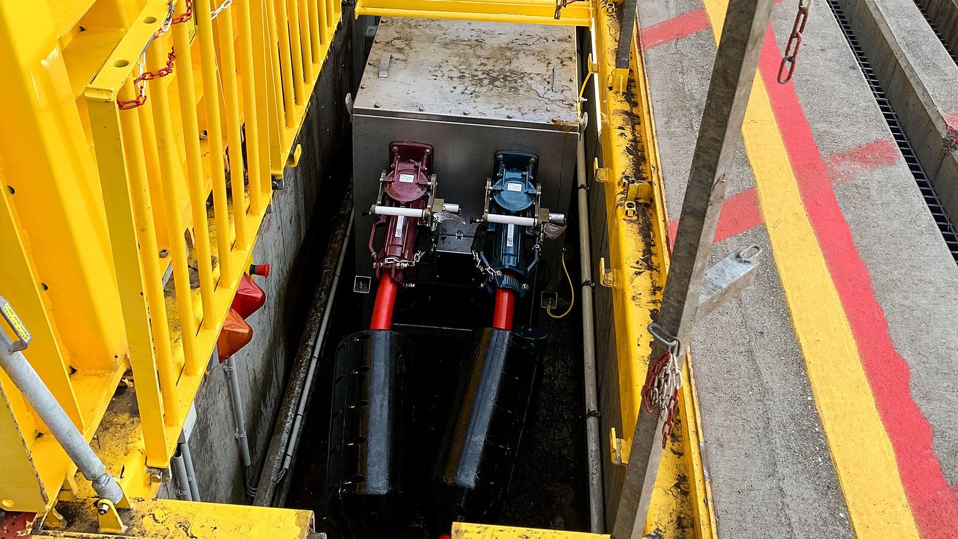 A top-down view of an industrial pit with yellow safety barriers containing machinery and cords
