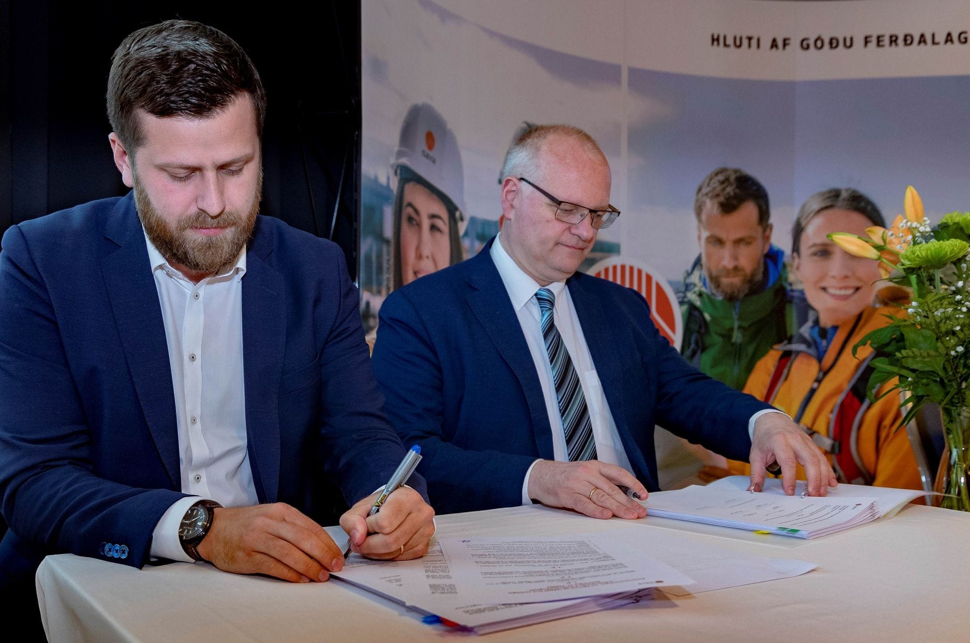 Photo of two men, one signing a document, most likely a contract