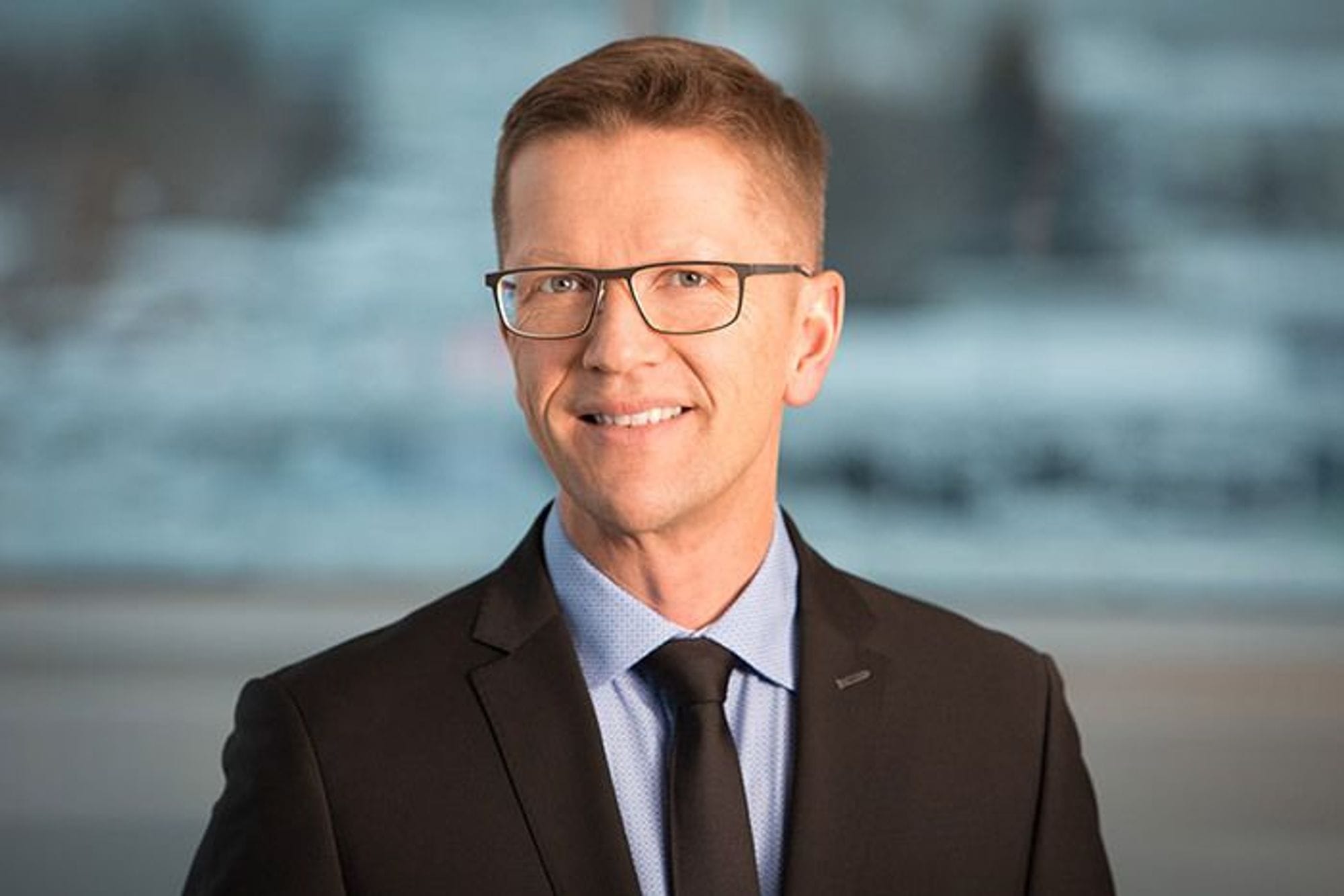 A man in black suit and glasses posing with a smile