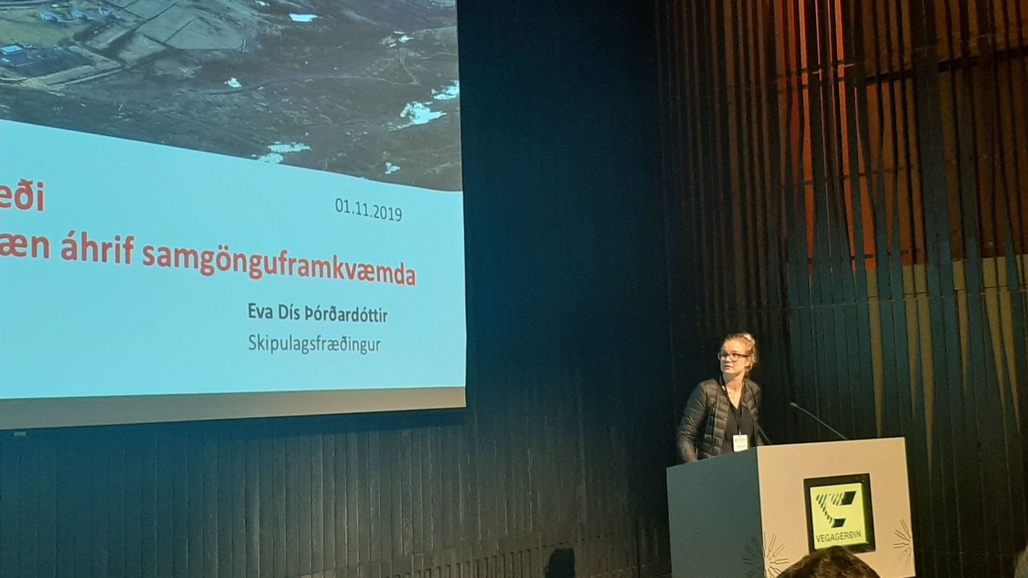 A woman presenting next to a large screen 