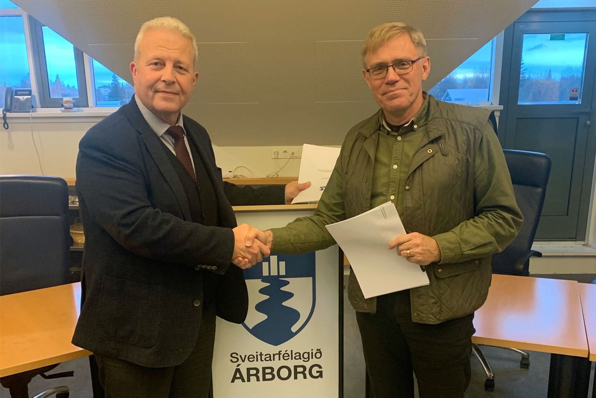 Two men shaking hands, holding documents
