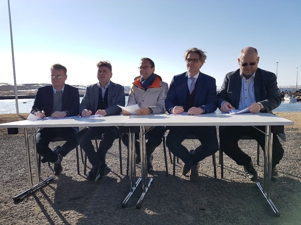 Five men in business attire sitting at a long table outdoors