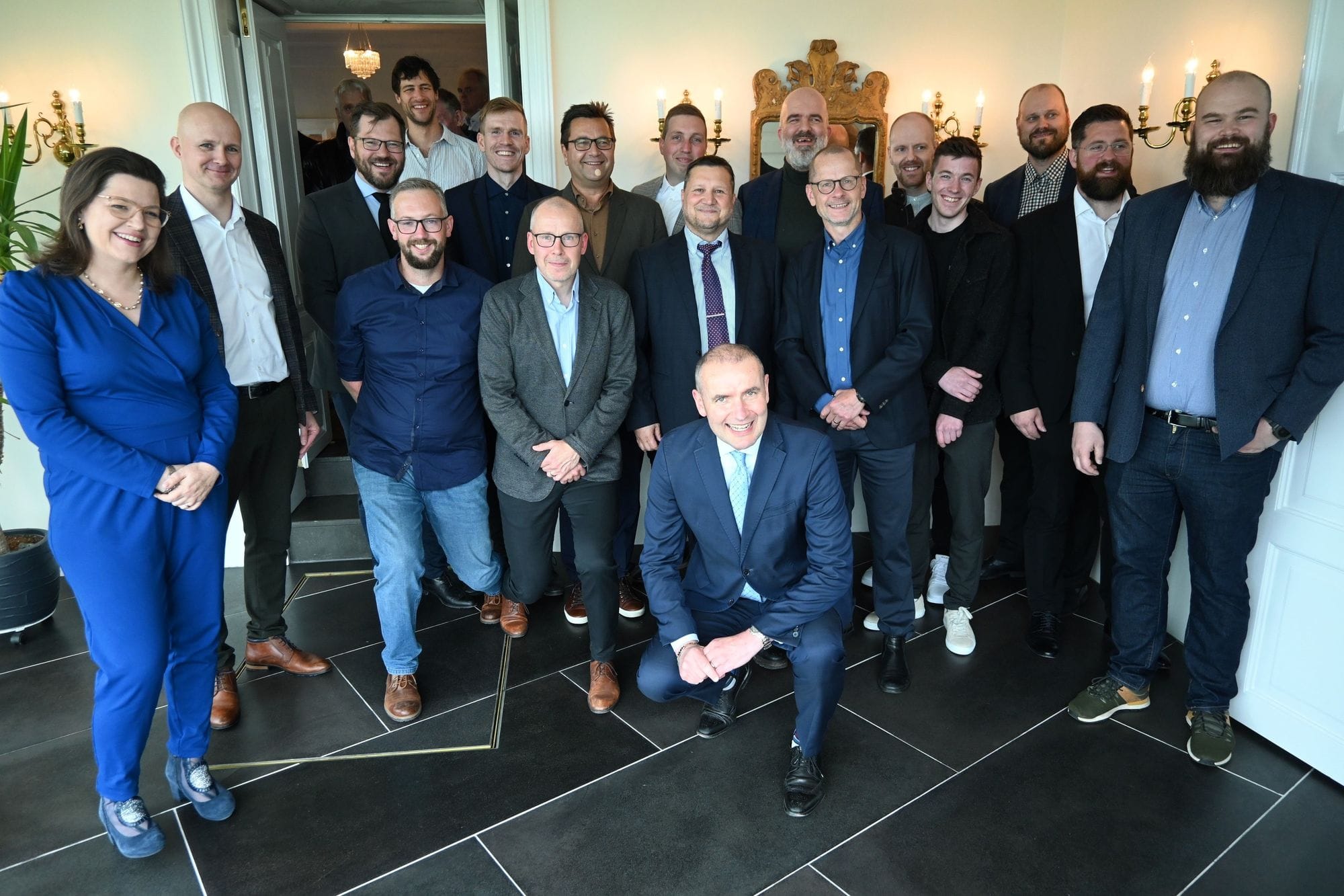 Around 16 employees pose for a group photo shoot with the President and First Lady of Iceland in a space with black tiles, white walls and gold decorations on the walls