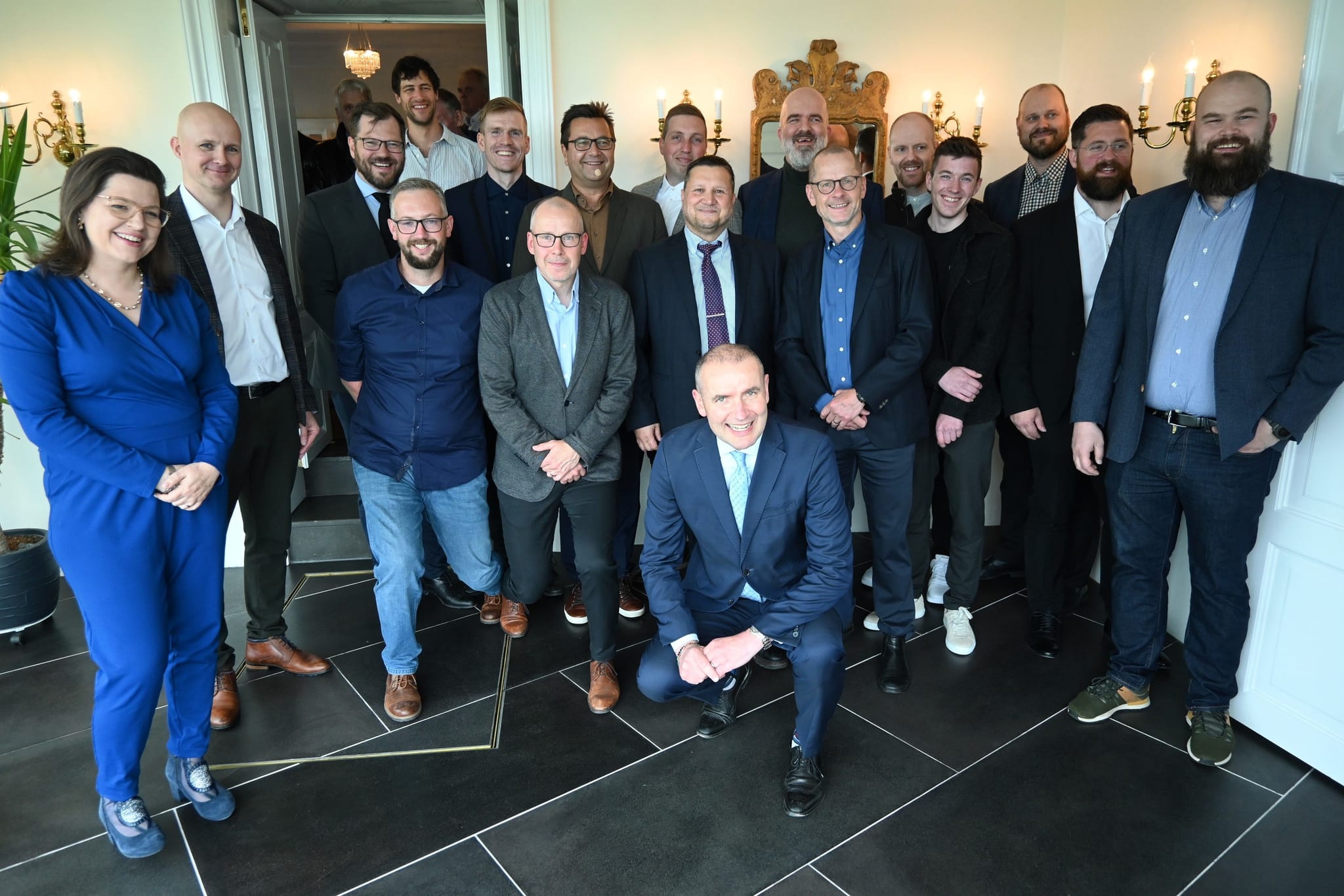 Around 16 employees pose for a group photo shoot with the President and First Lady of Iceland in a space with black tiles, white walls and gold decorations on the walls